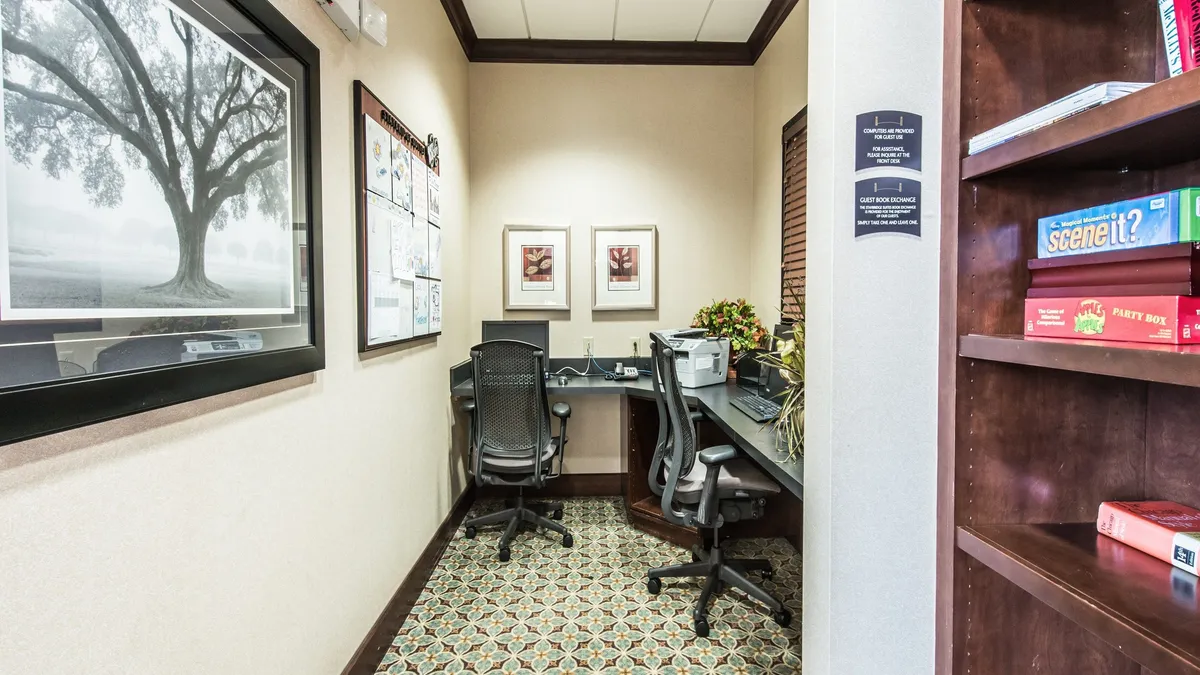 A dedicated workspace within a suite, featuring an office desk, modern artwork, and a bookshelf filled with books. The area is well-lit and designed for productivity, offering a comfortable environment for guests who need to work or plan during their stay.