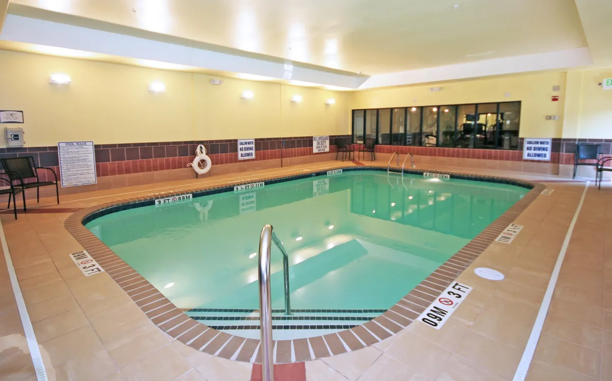 Showcasing another angle of the indoor swimming pool, this image emphasizes the pool ladder, adjacent seating, and a bright, airy setting. The scene conveys a refreshing and social environment, ideal for family gatherings, casual swims, or unwinding with a drink poolside.