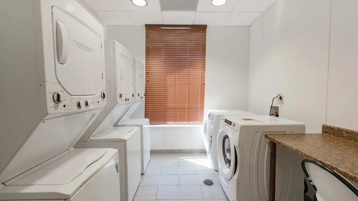 This image features a functional laundry room equipped with stacked washer and dryer units, an open countertop space for folding or sorting clothes, and a window with blinds that lets in natural light. The organized space conveys efficiency and modern convenience, making it easy for guests to handle their laundry needs during their stay.