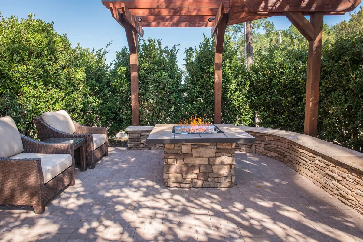 A cozy outdoor scene featuring a fire pit surrounded by a comfortable seating area beneath a pergola, framed by lush greenery. The space is designed for relaxation, socializing, and enjoying the outdoors, ideal for families to unwind together after a day of adventure.